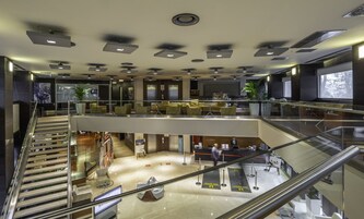 A modern hotel lobby with a glass railing, multiple seating areas, and a reception desk.