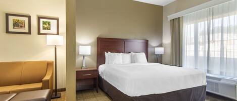 A hotel room with a large bed, a nightstand, a lamp, a sofa, and framed pictures on the wall.