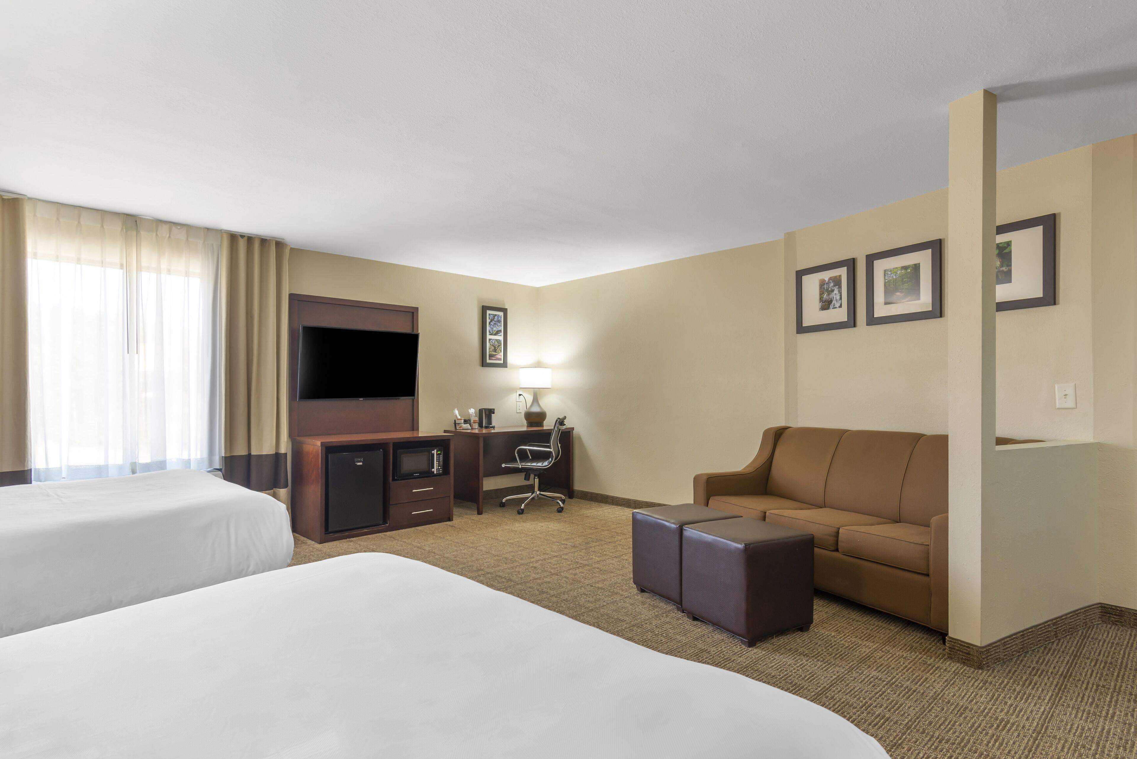 A hotel room with two beds, a desk with a chair, a sofa, a TV, and framed pictures on the wall.