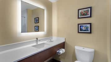 Un baño con lavamanos blanco, un espejo, dos cuadros enmarcados en la pared y un inodoro.