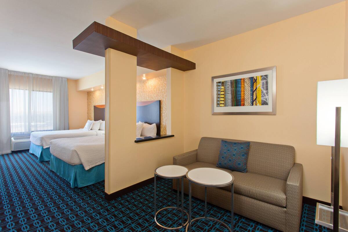 A hotel room with two beds, a sofa, two small tables, and a framed artwork on the wall.