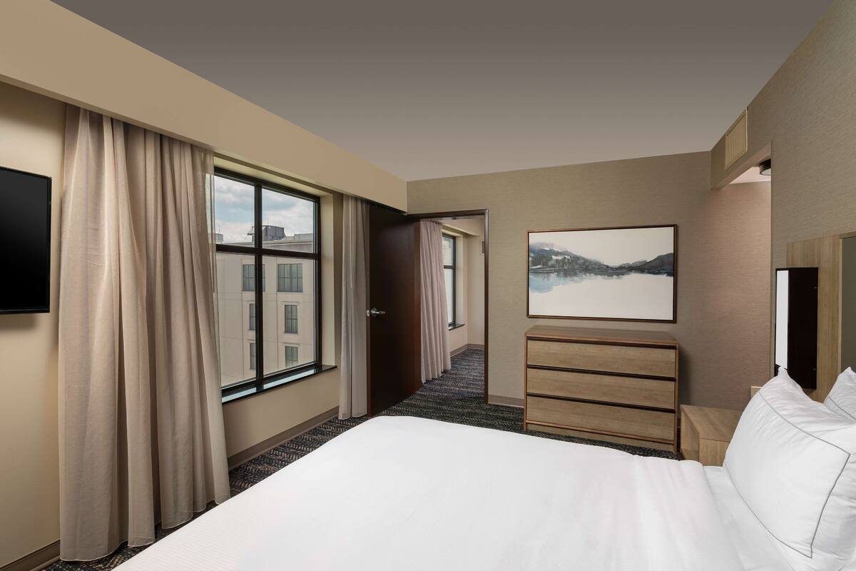 Une chambre d’hôtel avec un grand lit, un téléviseur à écran plat, une commode en bois et un tableau représentant un paysage de montagne.