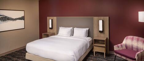 A hotel room with a large bed, a chair, a nightstand, and a wall-mounted lamp.