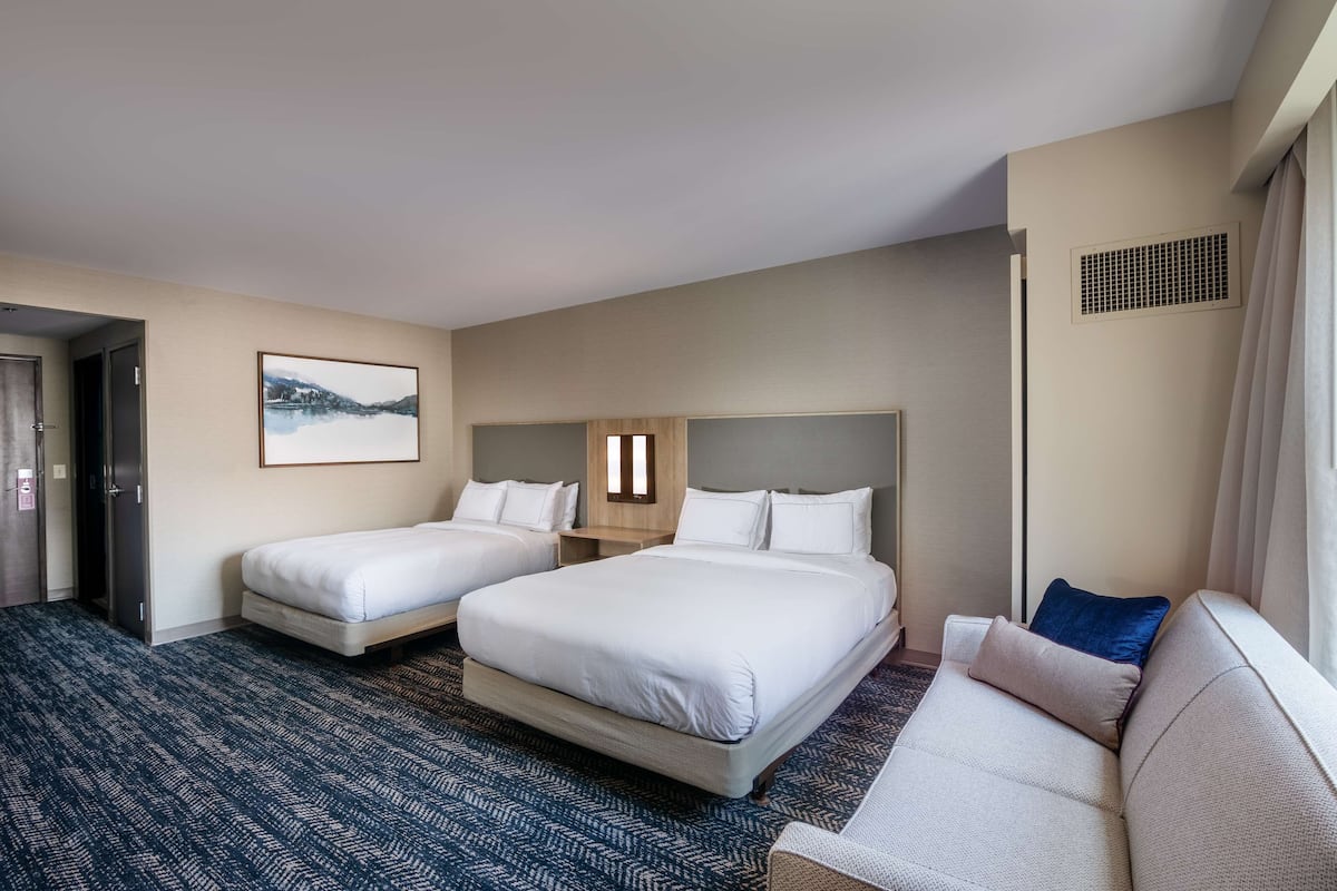 Une chambre d’hôtel avec deux lits, un canapé, une grande fenêtre et un tableau au mur.