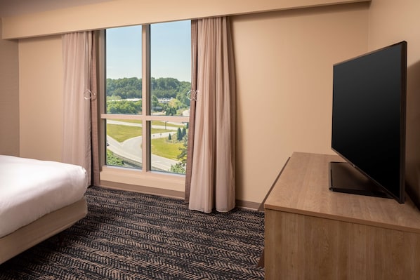 A hotel room with a large window, a bed, a TV, and a desk.