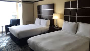 A hotel room with two beds, a desk, a chair, a lamp, and a window.