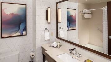 A modern bathroom with a large mirror, a sink, and a toilet. There are towels and toiletries on the sink counter.