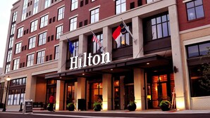 Hilton-hotelli, jossa on moderni julkisivu, useita ikkunoita ja kyltti, joka osoittaa, että hotellissa on tarjolla valvomapalvelu.