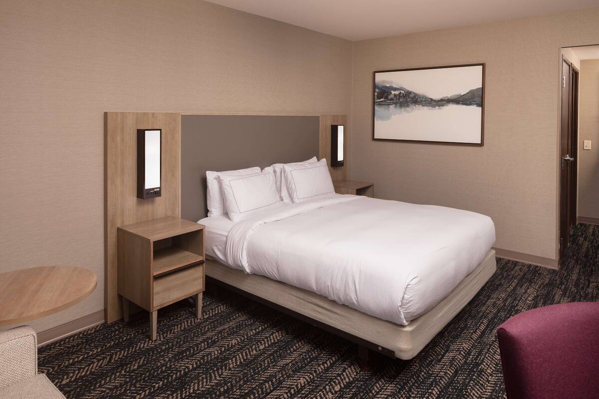 Une chambre d’hôtel avec un grand lit, une table de chevet en bois, une petite table et un téléviseur fixé au mur.