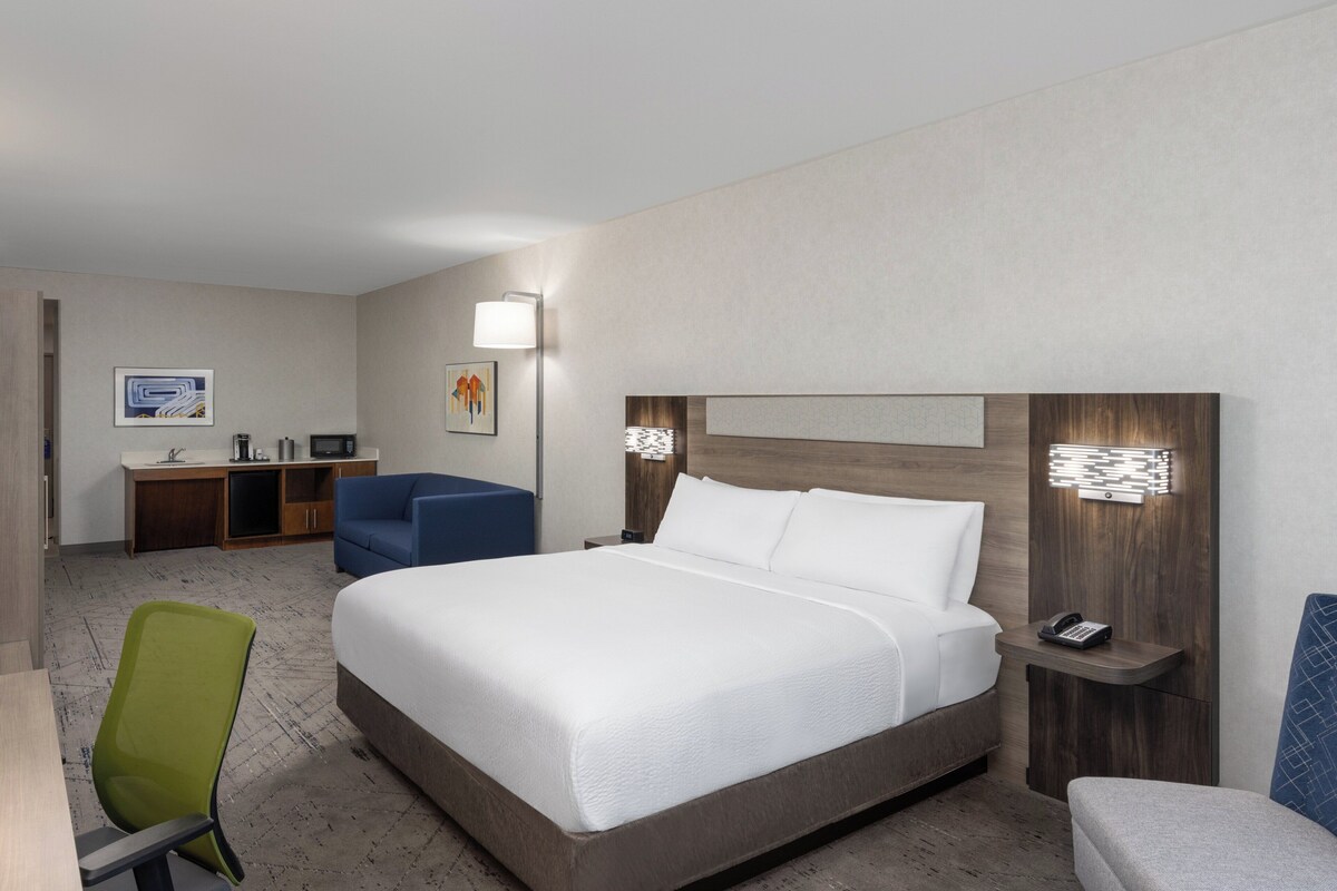 Ein Hotelzimmer mit einem großen Bett, einem Schreibtisch mit Stuhl, einem kleinen Tisch und einer Couch.