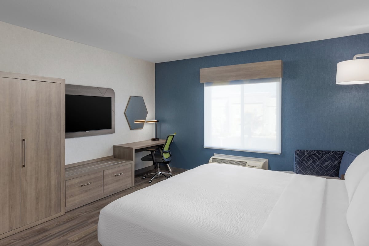 Una camera d'albergo con un letto, una scrivania, una sedia, una televisione e una finestra.