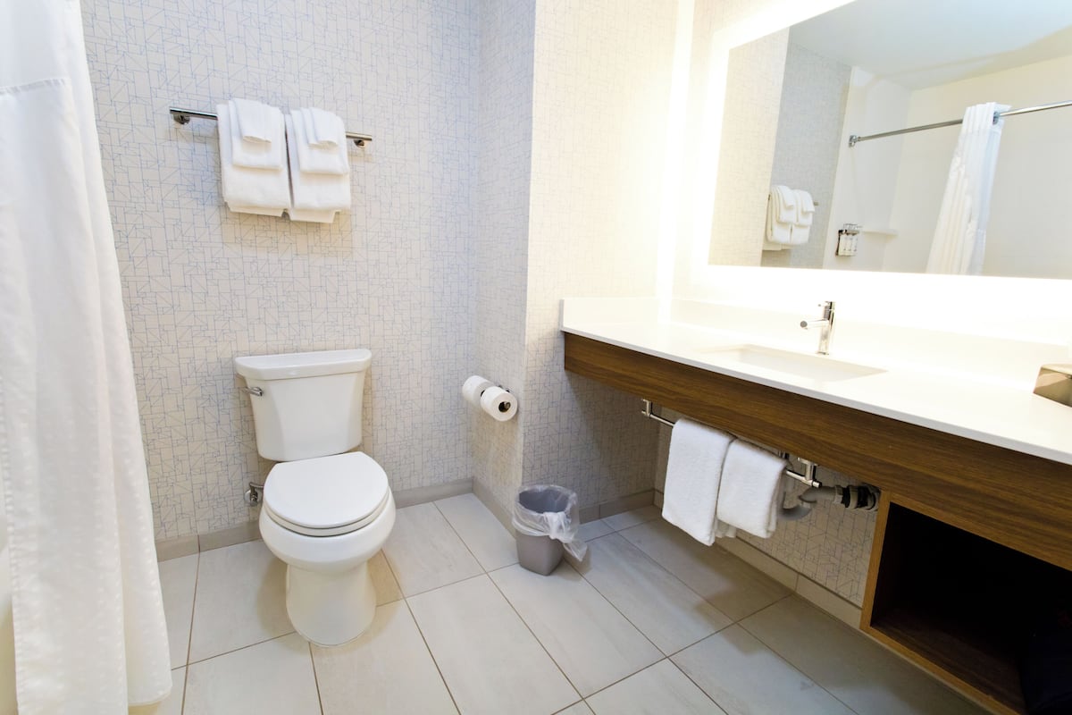 Un bagno moderno con il water, un lavandino e uno specchio. Asciugamani su un portasciuga e un cestino.