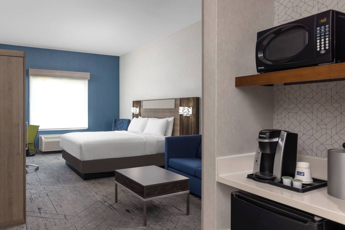 Camera d'albergo con un letto, una scrivania, una sedia, un forno a microonde, una macchina per il caffè e un piccolo frigorifero.