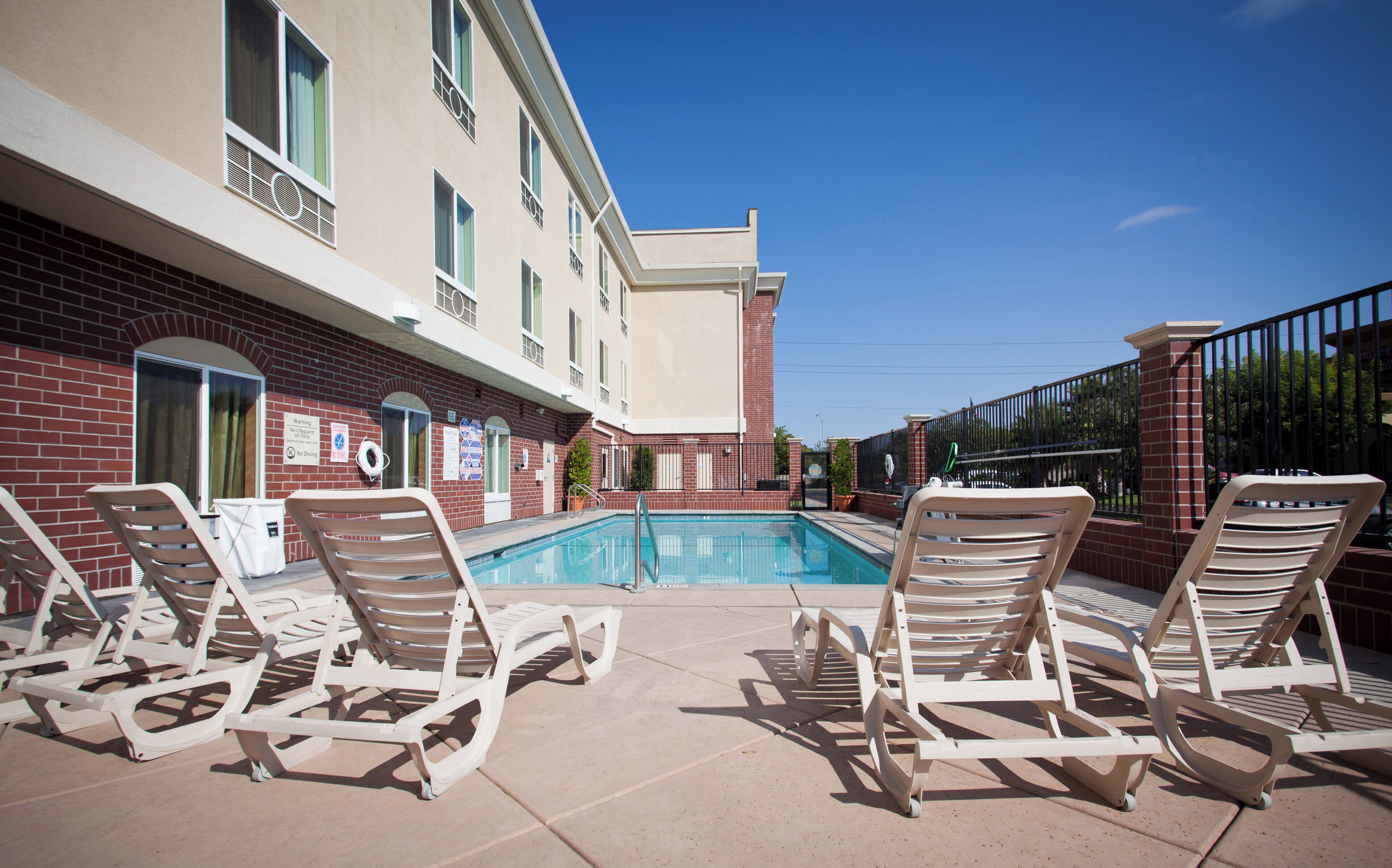 A poolside area with lounge chairs, a swimming pool, and a building with multiple windows and a brick facade.