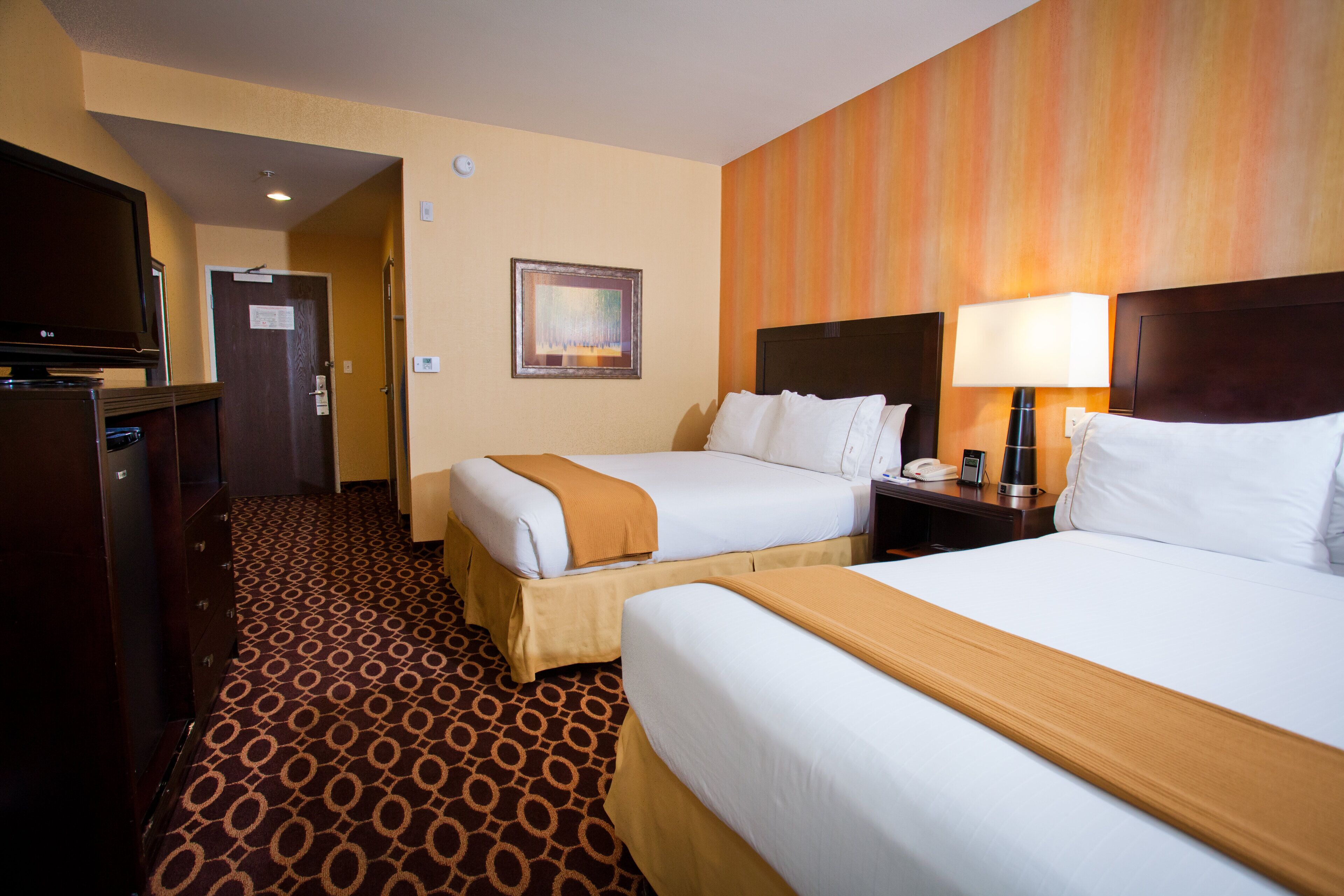 A hotel room with two beds, a TV, a lamp, and a painting on the wall.