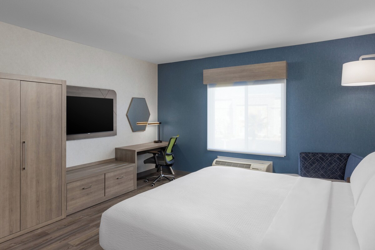 Ein Hotelzimmer mit einem Bett, einem Schreibtisch, einem Stuhl, einem Fernseher und einem Fenster.
