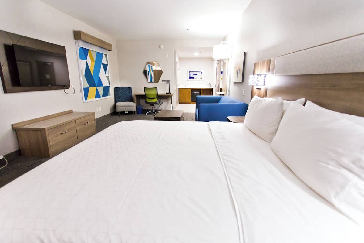 Una camera d'albergo con un letto grande, una scrivania con un computer, una sedia e una TV fissata al muro.