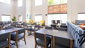 Een ruime eetruimte met meerdere tafels en stoelen, grote ramen en een modern plafondontwerp.