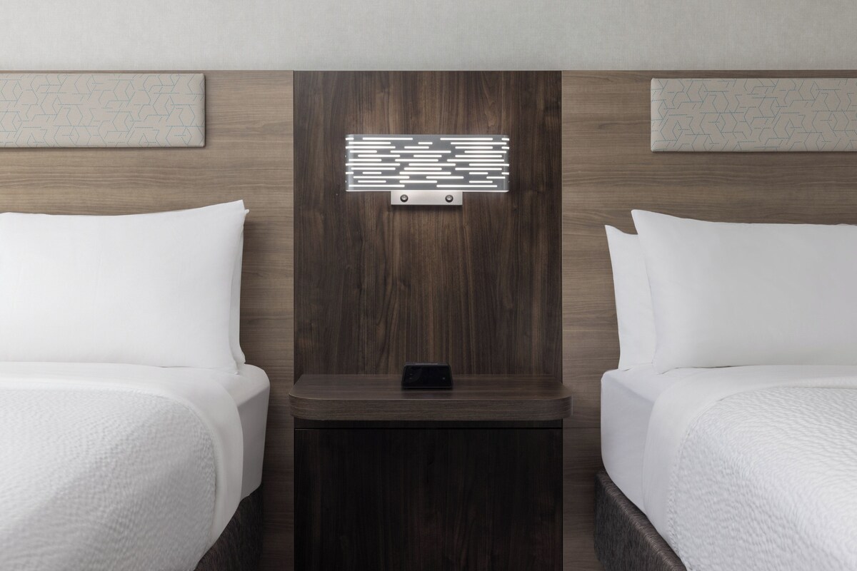 Ein Hotelzimmer mit zwei Betten, einem Holzkopfende, einem Nachttisch mit Telefon und einer Wandleuchte.
