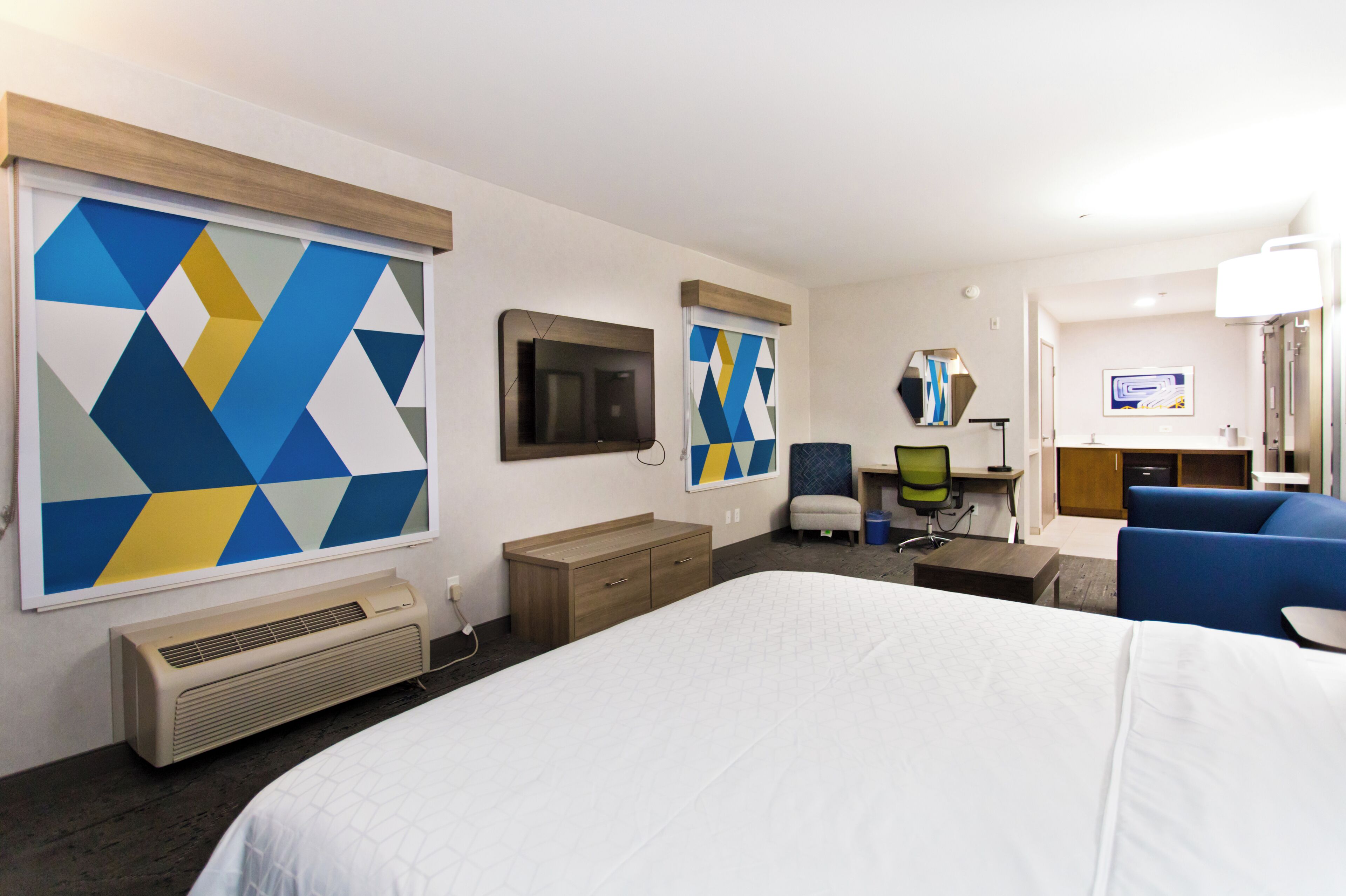 A hotel room with a large bed, a desk with a computer, a chair, a small table, and a TV.