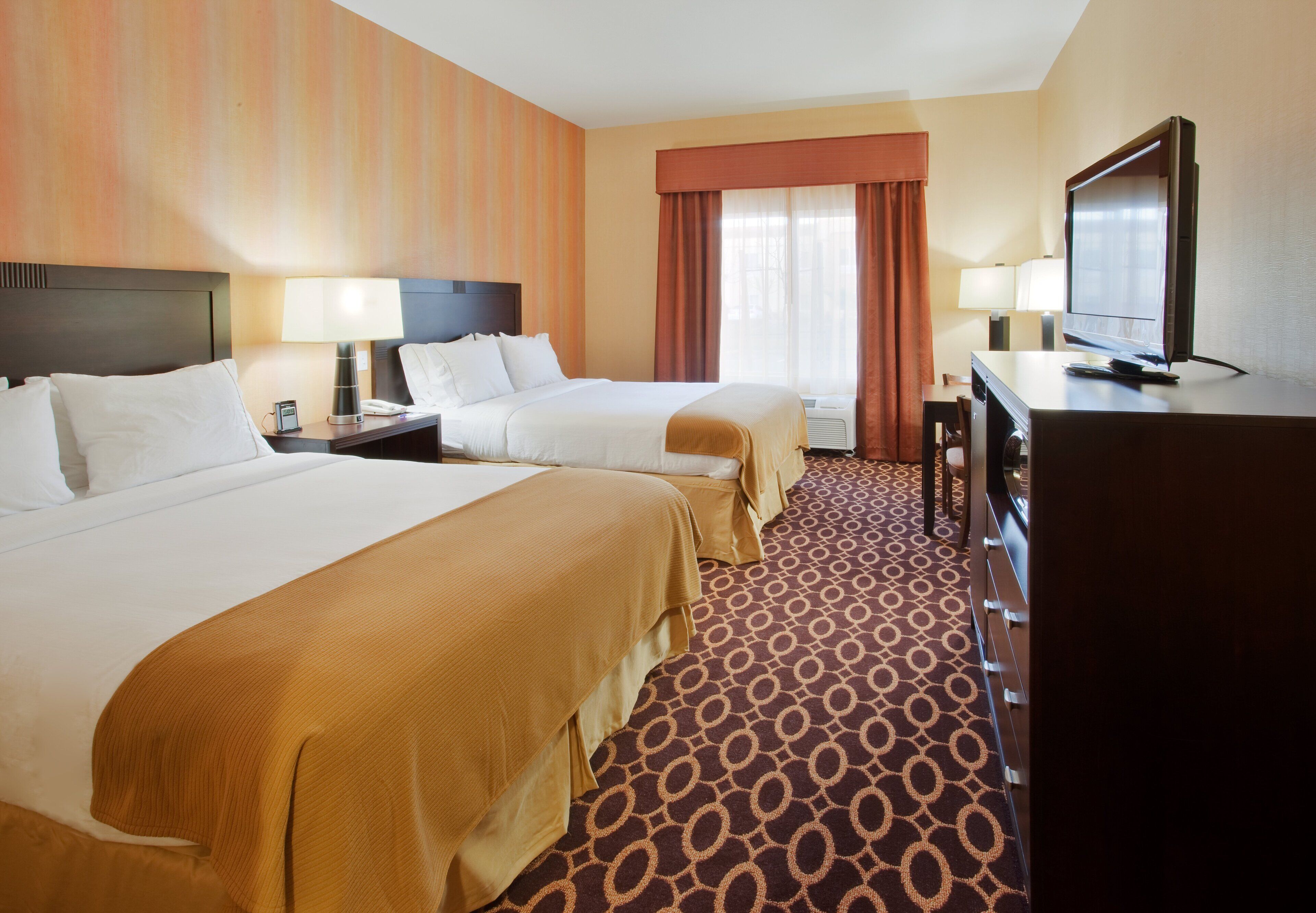 A hotel room with two beds, a television, a desk, and a window with curtains.