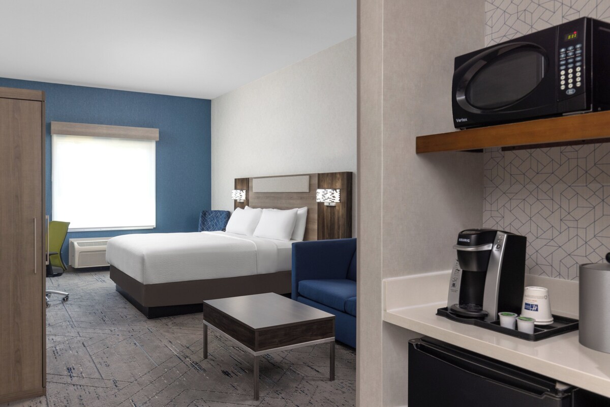 Ein Hotelzimmer mit Bett, Schreibtisch, Stuhl, Mikrowelle, Kaffeemaschine und kleinem Kühlschrank.