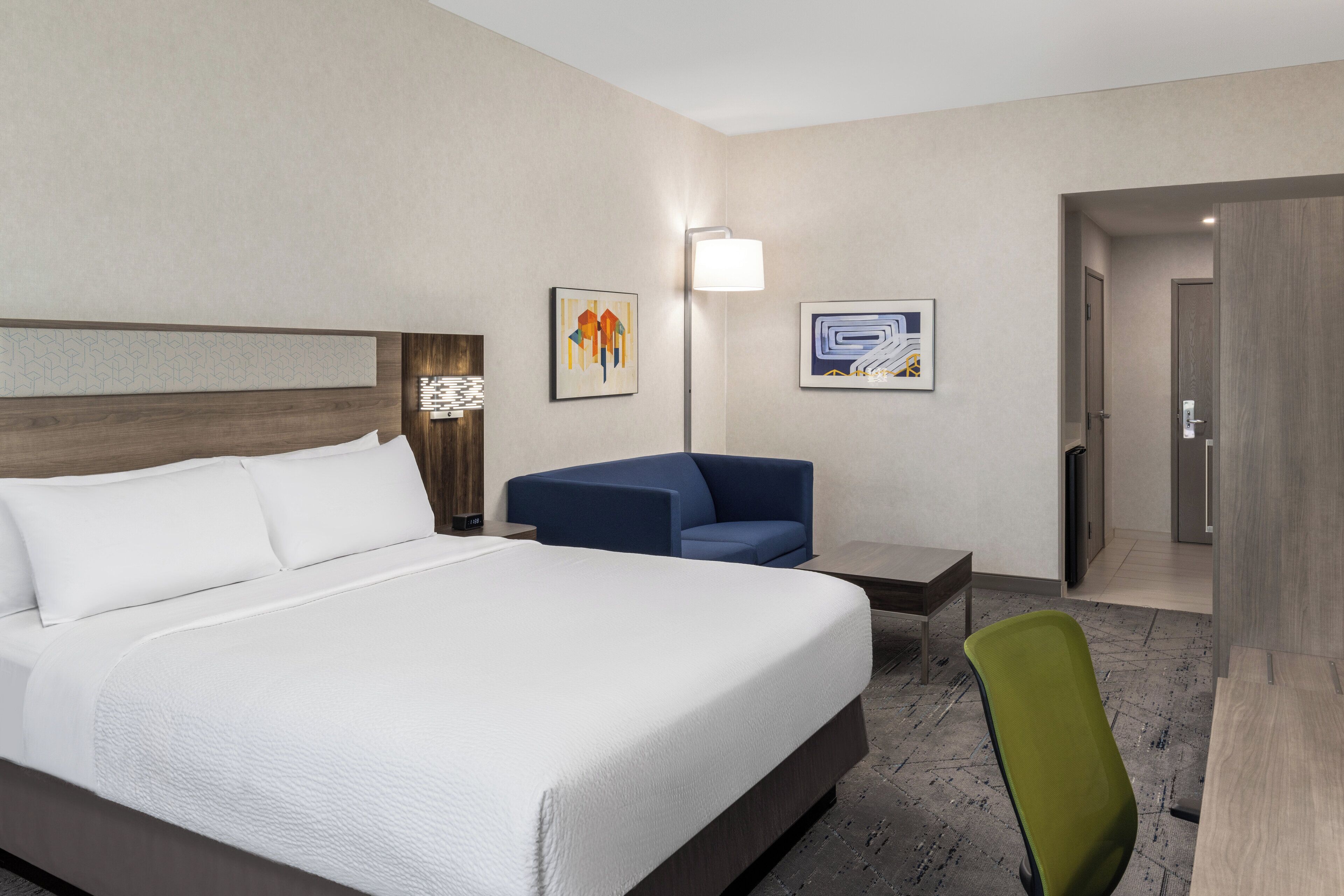 A hotel room with a large bed, a blue sofa, a small table, and a green chair.
