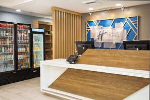 Ein Hotelrezeptionstresen mit Holzoptik, ein Coca-Cola-Kühlschrank und ein digitales Display.