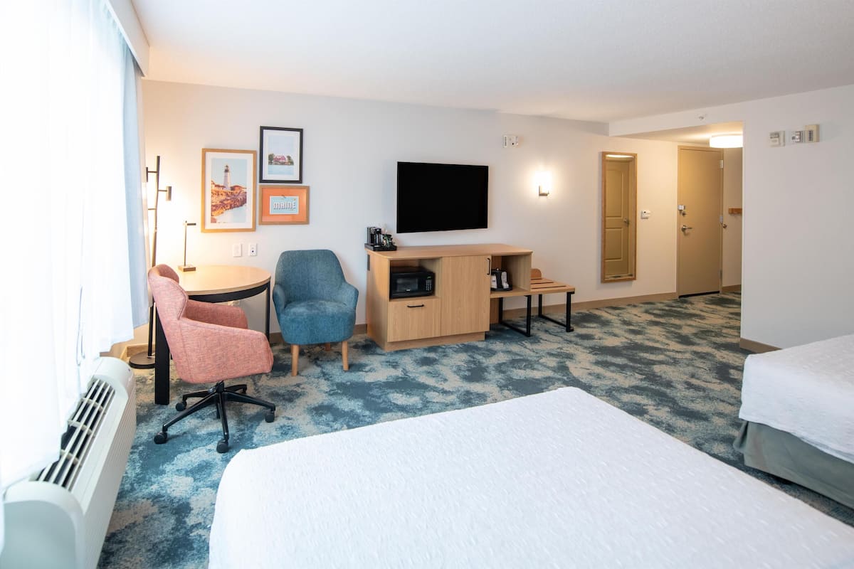 A hotel room with a bed, a desk with a computer, a chair, a television, and a door.
