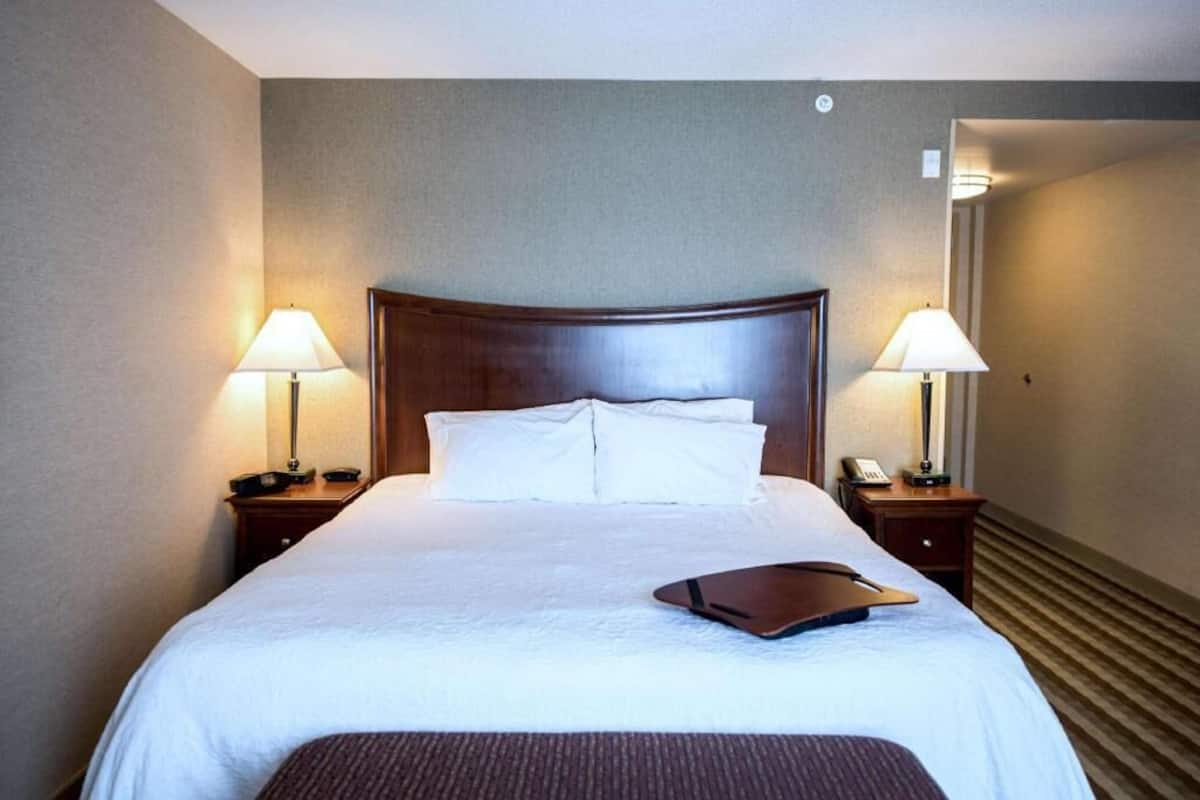 A hotel room with a large bed, two bedside tables with lamps, a nightstand with a phone, and a carpeted floor.