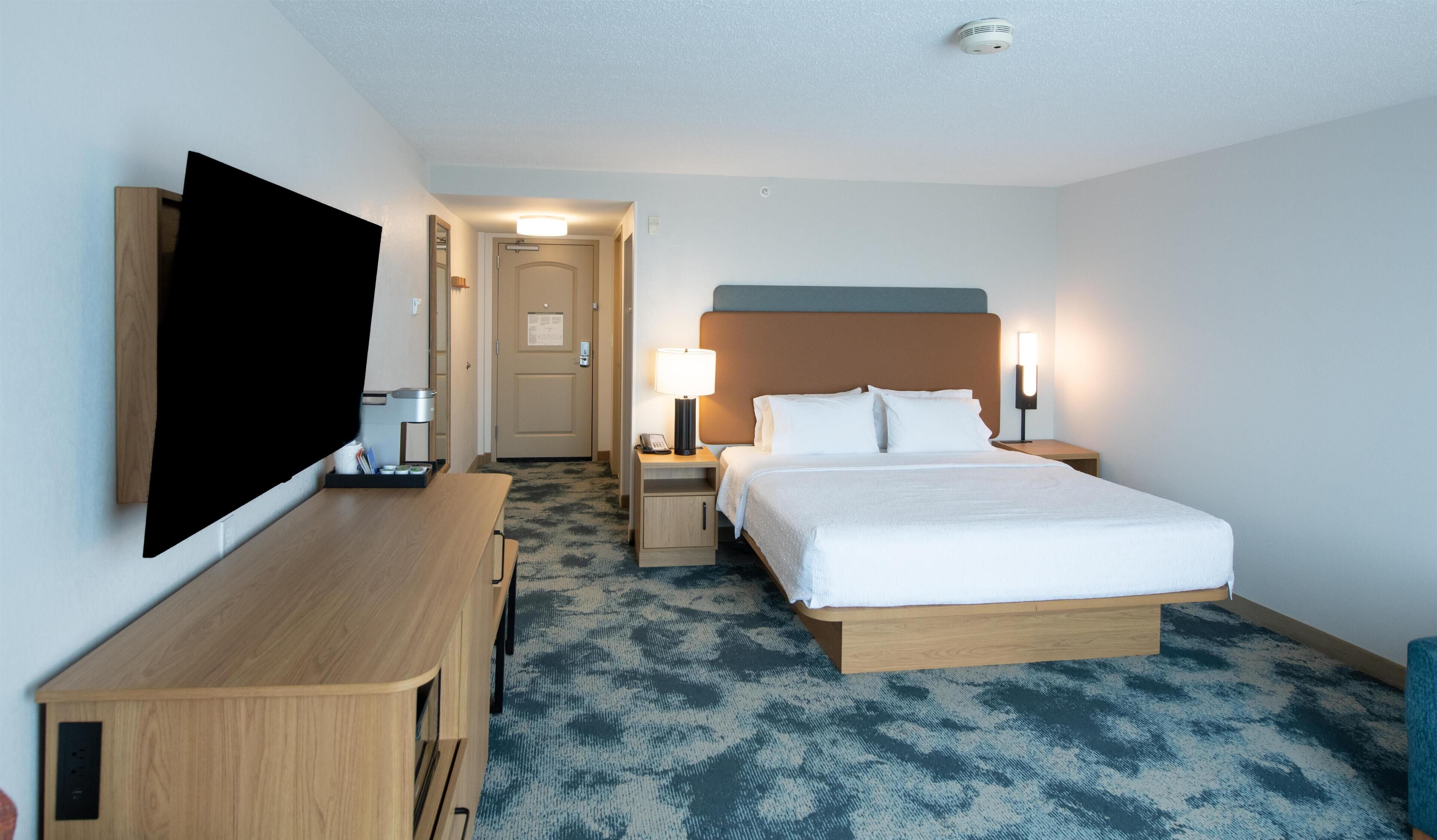 Une chambre d’hôtel comprenant un lit, des tables de chevet, un bureau, un téléviseur à écran plat et un sol recouvert de moquette.
