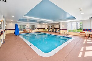 Una piscina con solárium empinado, tumbonas y una zona cubierta con toldo azul.