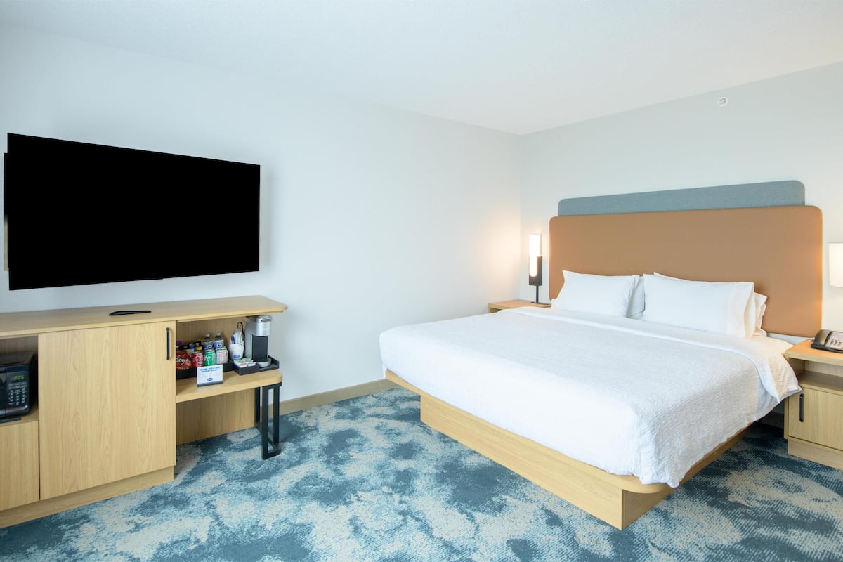 A hotel room with a bed, bedside tables, a flat-screen TV, a microwave, and a coffee machine.