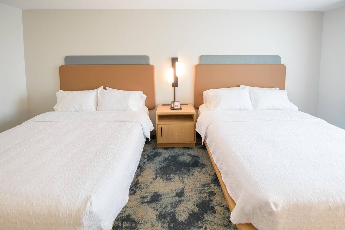 A hotel room with two beds, a nightstand with a lamp, and a patterned rug.