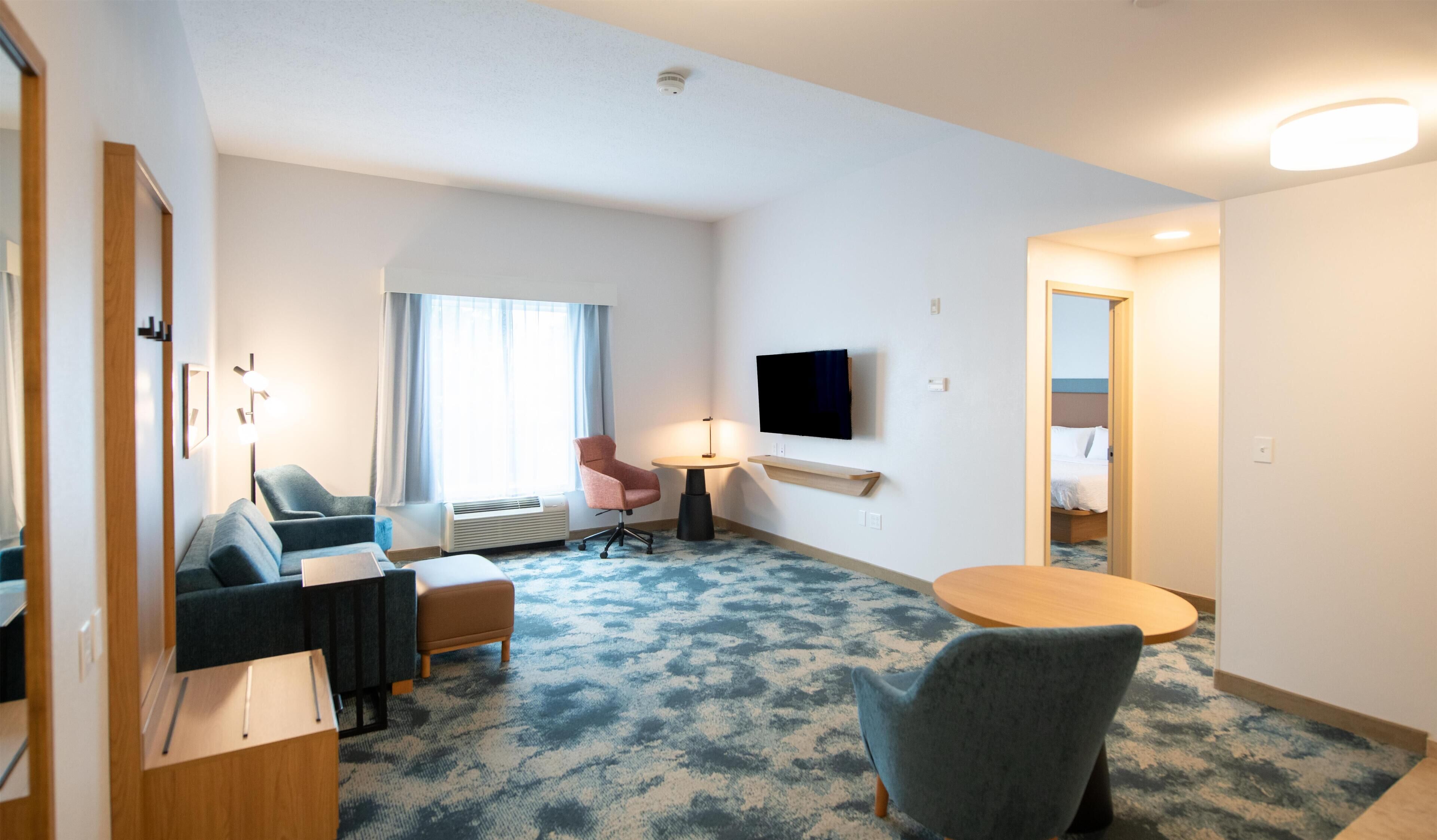 A hotel room with a sofa, a chair, a small table, a TV, and a bed.