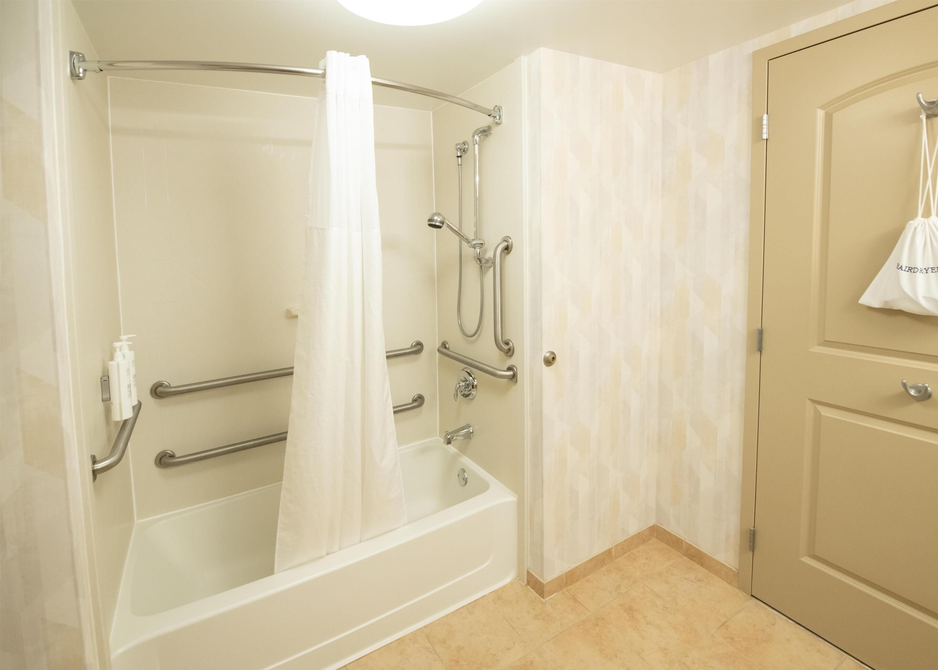 A bathroom with a walk-in shower, grab bars, a bathtub, and a door with a towel hanging on it.
