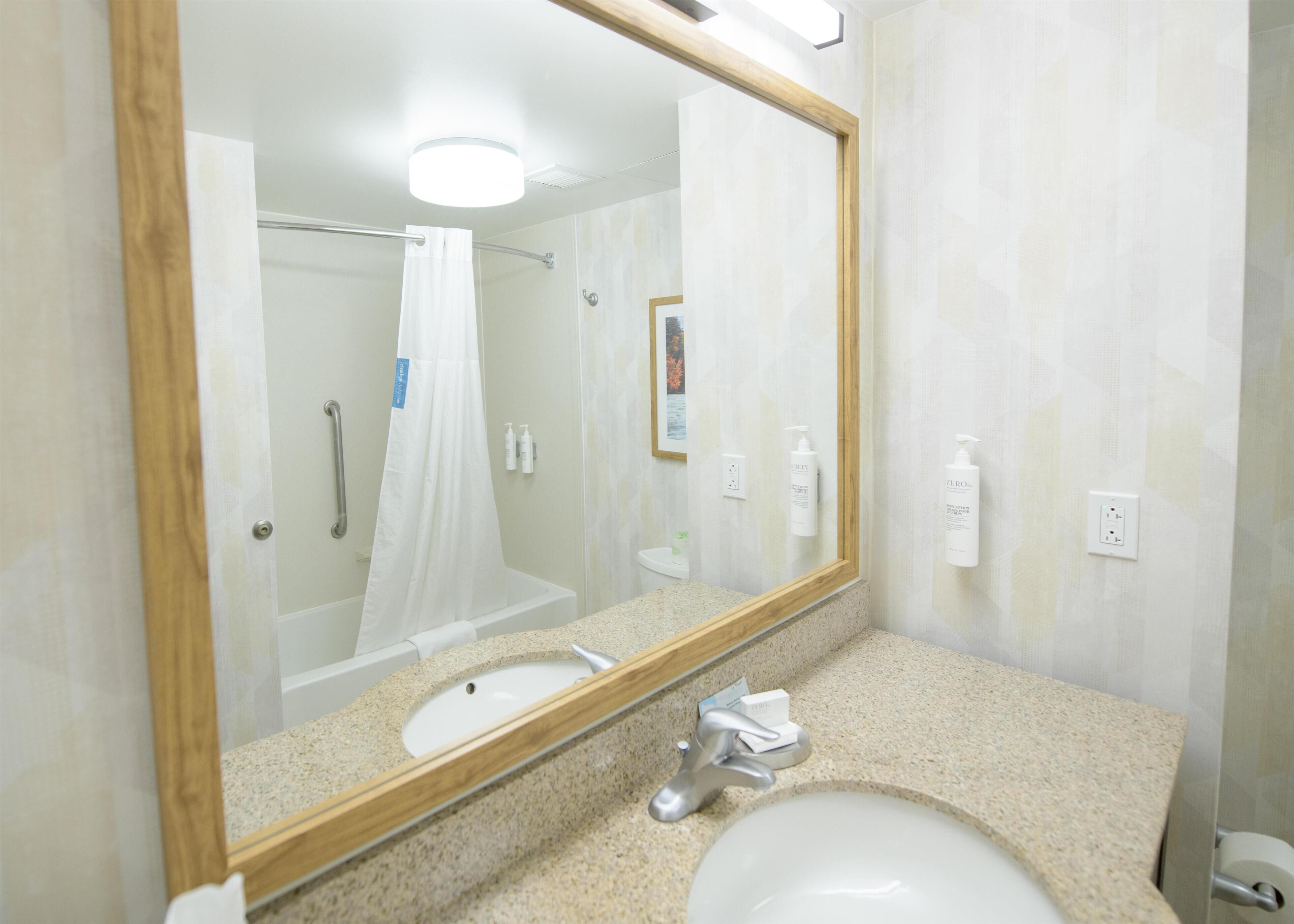 A bathroom with a large mirror, a sink, a shower, and toiletries on the wall.