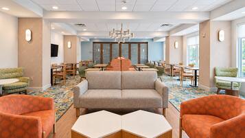 A hotel lobby with a central seating area, multiple tables, and chairs.