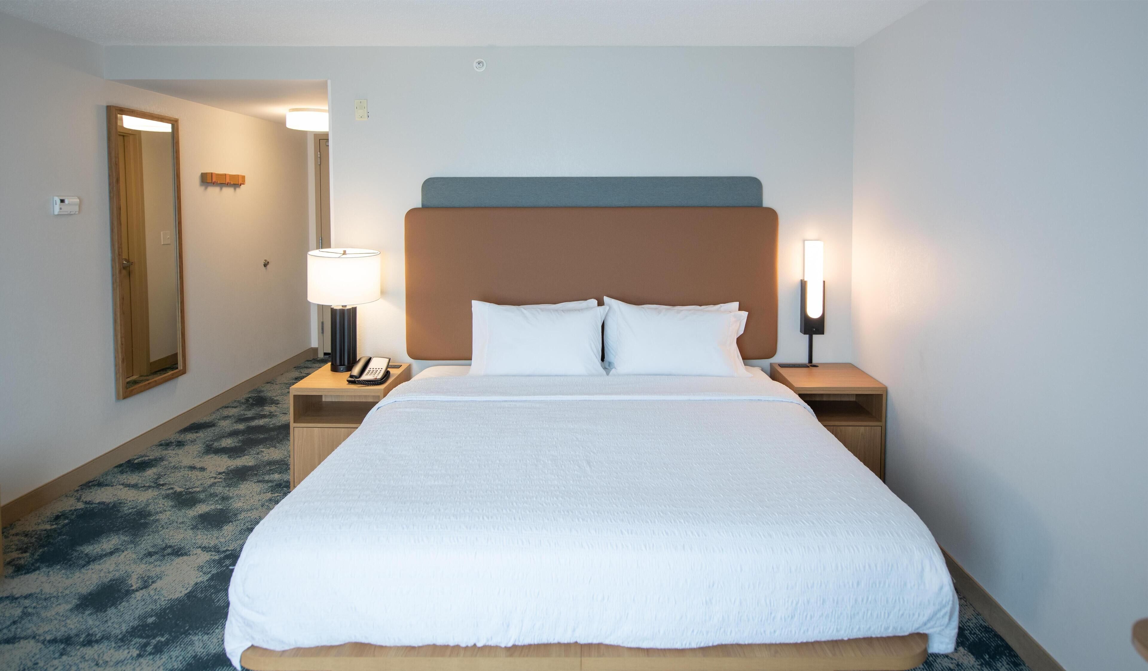 Ein Hotelzimmer mit einem großen Bett, zwei Nachttischen mit Lampen, einem Spiegel und einem Teppichboden.