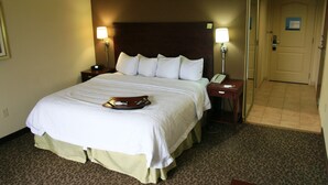 A hotel room with a large bed, two bedside tables, a nightstand, and a door. - Hampton Inn & Suites West Point (West Point)