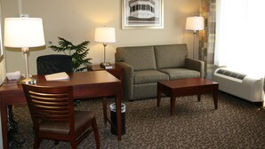 A hotel room with a sofa, two chairs, a desk with a lamp, a small table, a potted plant, and a framed picture on the wall. - Hampton Inn & Suites West Point (West Point)