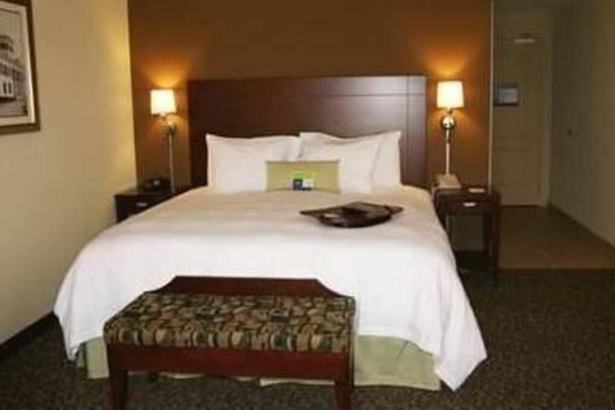 Habitación de hotel con cama, dos lámparas de noche, mesitas de noche y un pequeño banco.