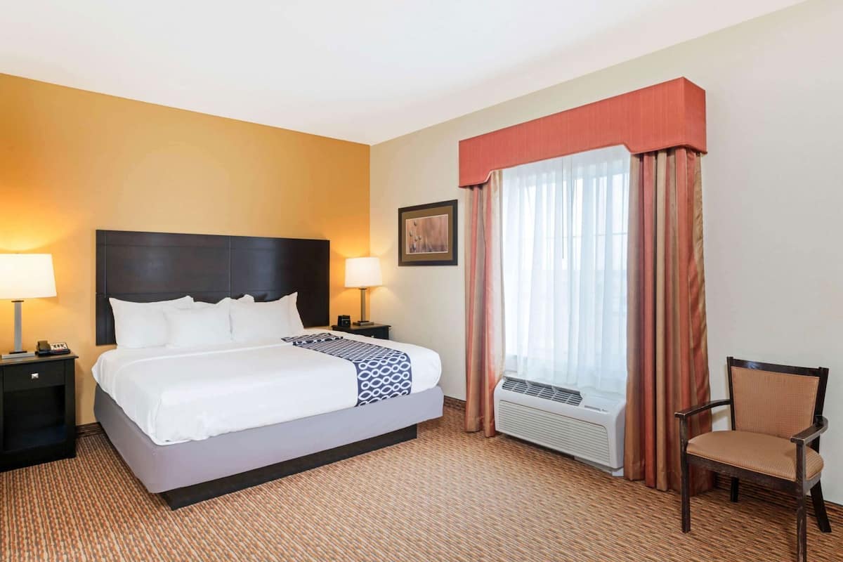 Een hotelkamer met een bed, twee nachtkastjes, een stoel, een raam met gordijnen en een wandairconditioner.