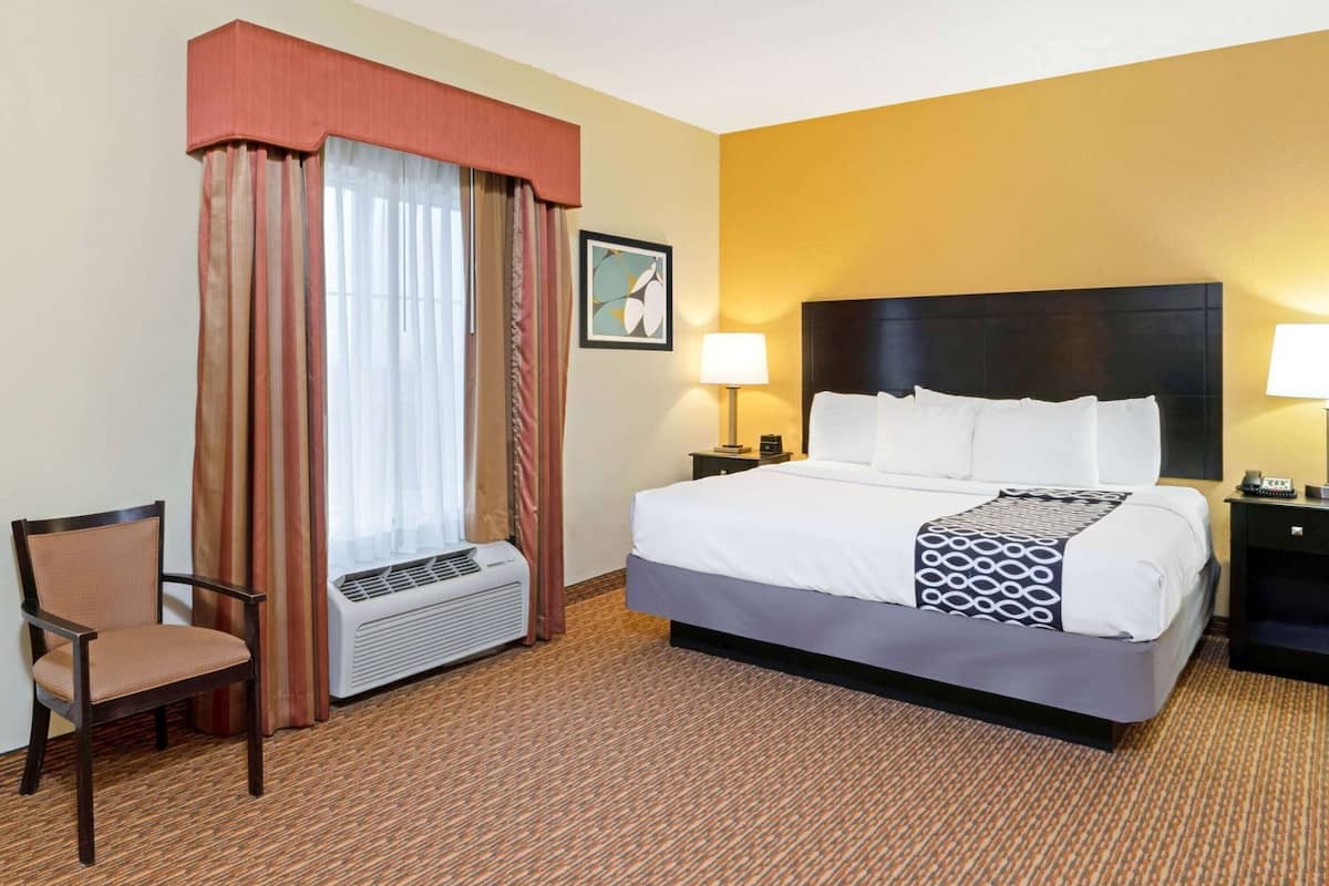 Hotelkamer met een bed, twee nachtkastjes, een stoel, een raam met gordijnen, een airconditioner en een aan de muur hangend schilderij.