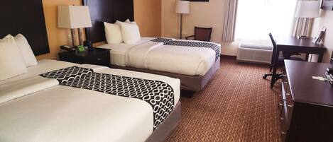 Una habitación de hotel con dos camas, un escritorio, una silla y una lámpara.