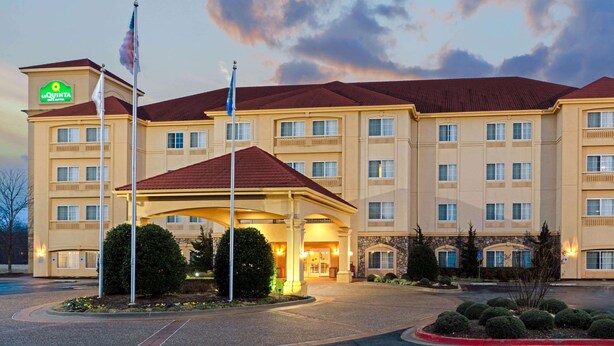 A hotel with a central entrance, multiple floors, and a flagpole with flags. - La Quinta Inn & Suites by Wyndham Stillwater-University Area (Stillwater)