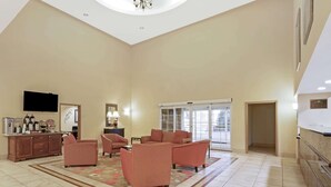 A spacious living area with a large sofa set, a flat-screen TV, and a kitchen area with a counter and appliances. - La Quinta Inn & Suites by Wyndham Stillwater-University Area (Stillwater)