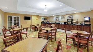 A hotel dining area with multiple tables and chairs, a kitchen counter, and a television. - La Quinta Inn & Suites by Wyndham Stillwater-University Area (Stillwater)