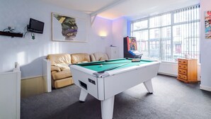 Une table de billard dans une pièce avec une fenêtre, un canapé et un téléviseur fixé au mur.