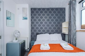 A hotel room with a bed, a nightstand, a radiator, a wall-mounted fan, and a window with curtains. - Derwent Hotel (Blackpool)